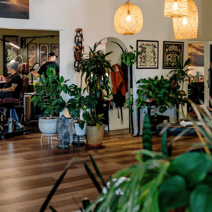 The interior of a tattoo shop, Twofold Tattoo. There are hardwood floors, plants, and art placed on the walls.