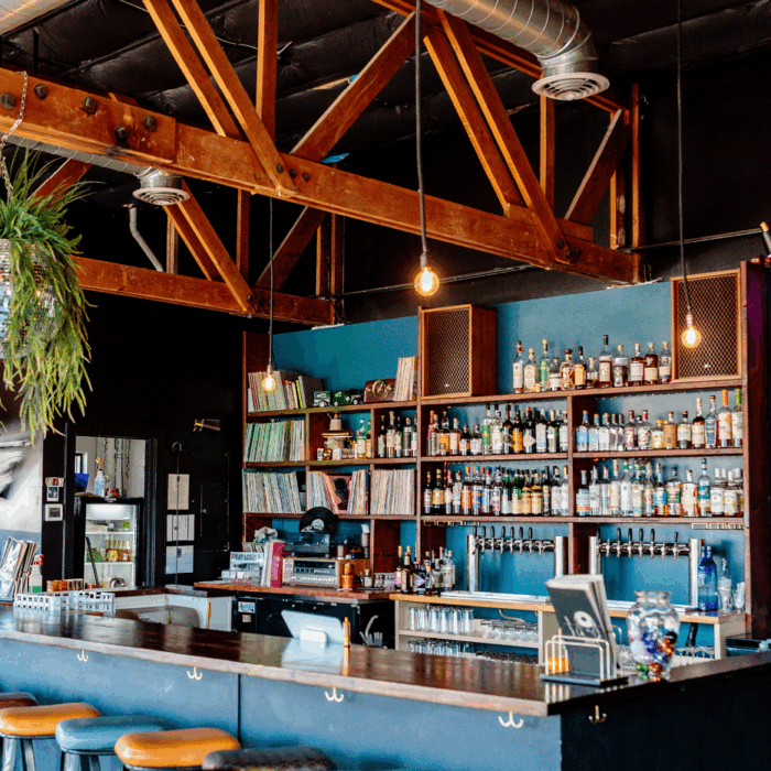 The inside of a bar, the back wall is full of a variety of alcohol and vinyls.