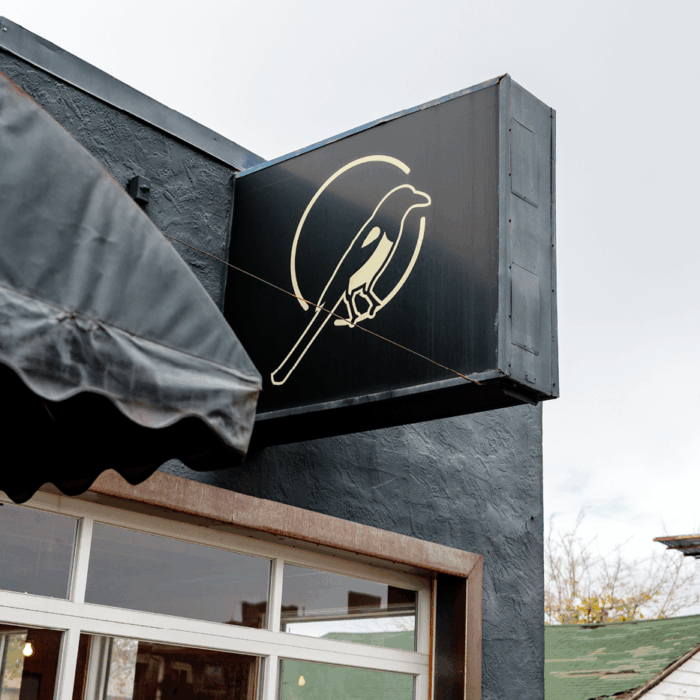 A black square sign with a magpie bird logo for Magpie Coffee Roasters.