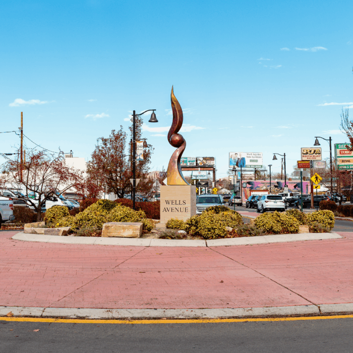 A statue with two abstract wavy shapes going up and down, between them is a round ball shape. It sits on top of a cement cube that reads, "Wells Avenue"